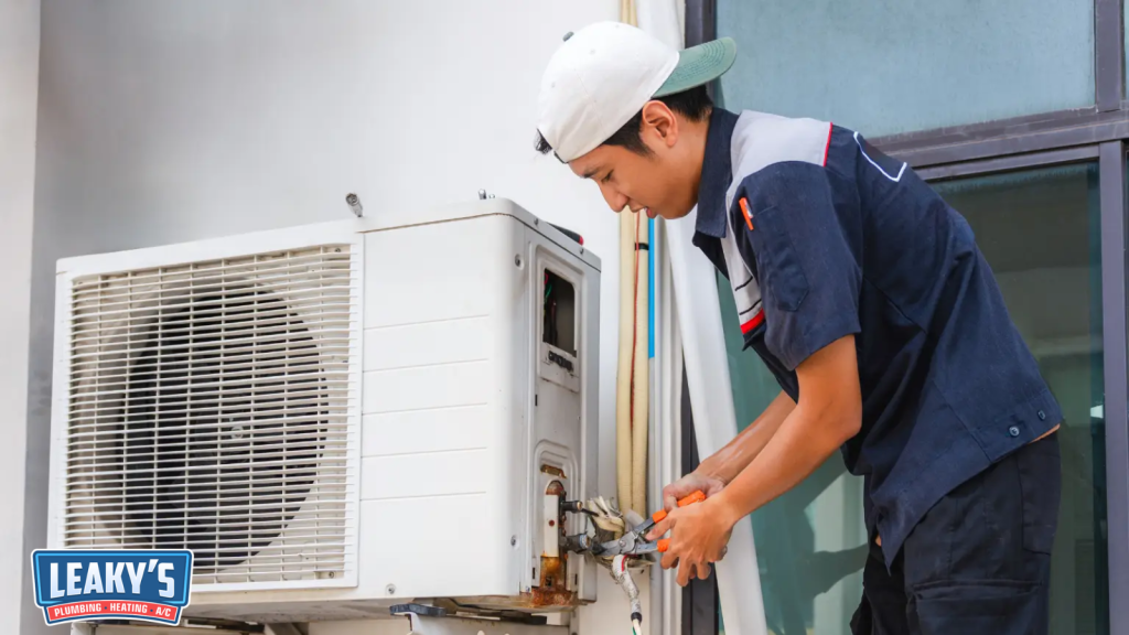 HVAC technician servicing an outdoor split HVAC condenser unit using tools during routine system maintenance.