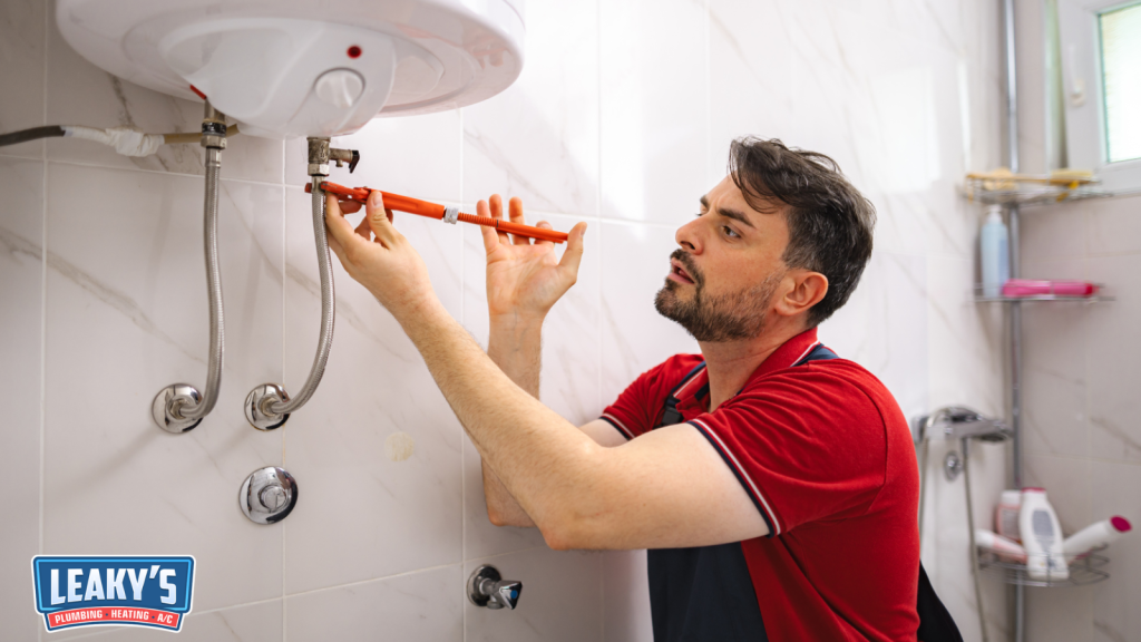 Plumber tightening a pipe connection while repairing a wall-mounted water heater inside a bathroom.