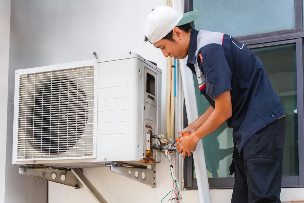 HVAC technician servicing an outdoor split HVAC condenser unit using tools during routine system maintenance.