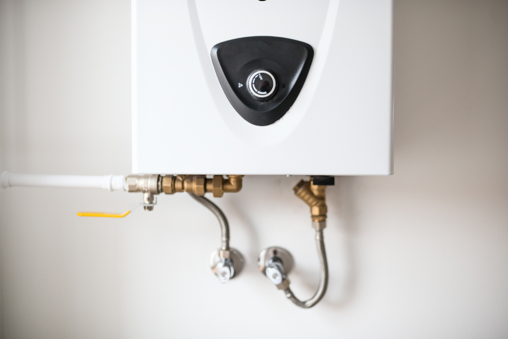 Wall-mounted residential water heater with visible plumbing connections and control dial installed in a home utility area.