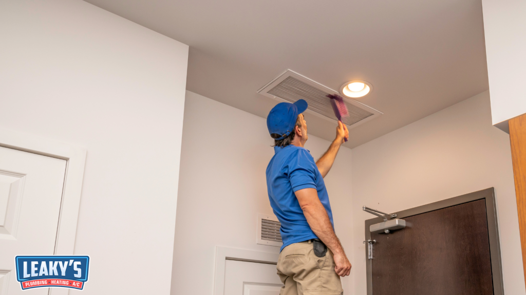 A maintenance technician cleaning an air vent on the ceiling of a residential room using a dusting tool during routine HVAC maintenance.